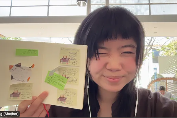 A young woman holds up a page of her journal and winks at the camera