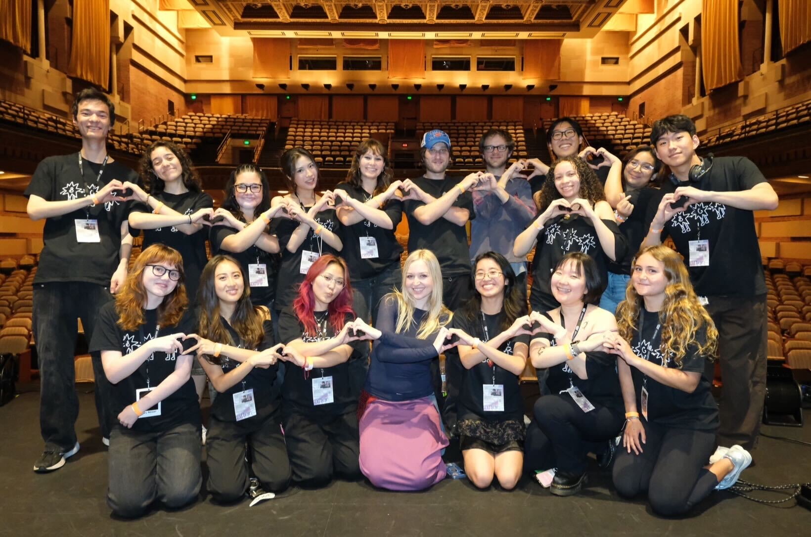 A group of UCLA students pose on stage after an event making heart shapes with their hands