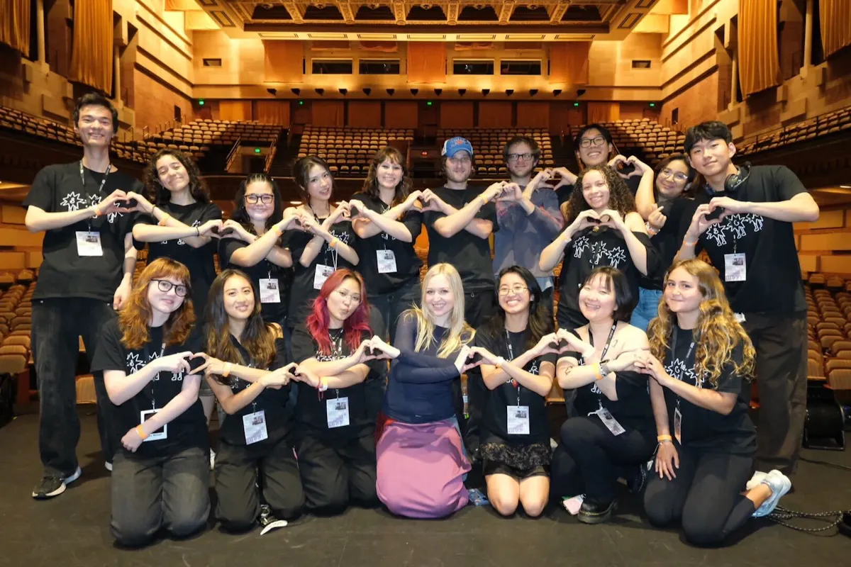 A group of UCLA students pose on stage after an event making heart shapes with their hands