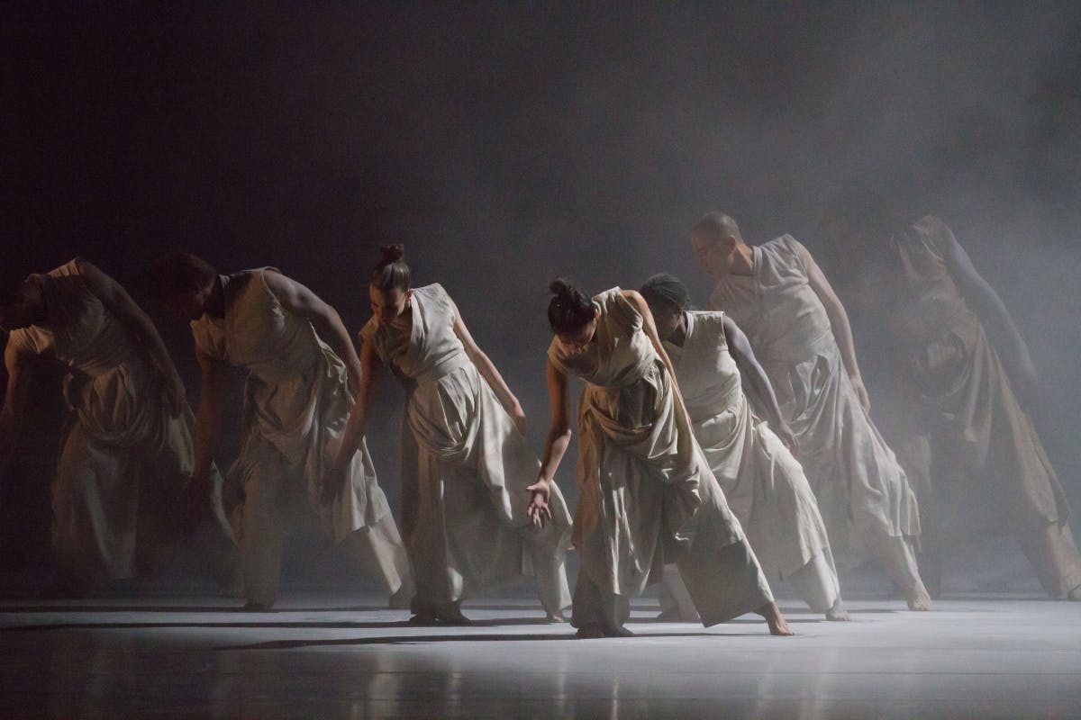 A stage full of dancers with a spotlighting and fog.