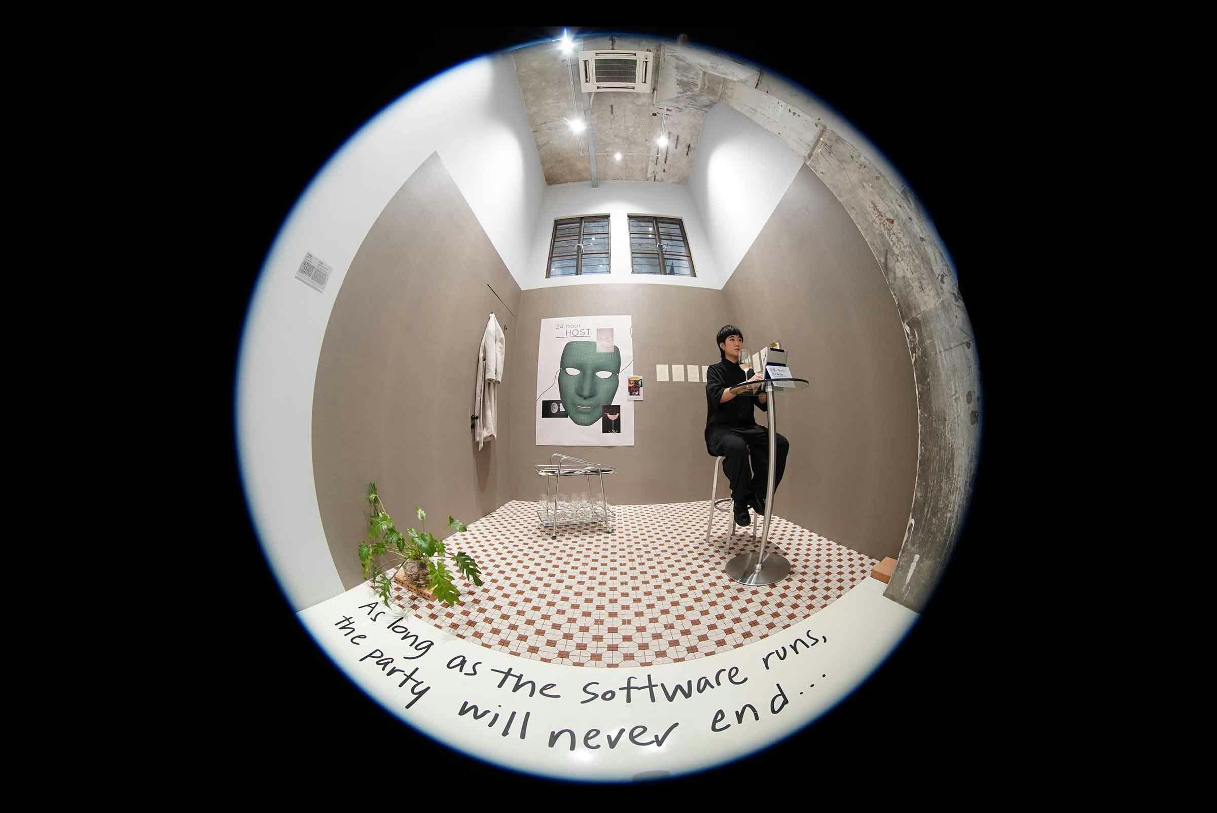 Fisheye lens image of an individual sitting at a small table in a small room with a plant and posters on the wall