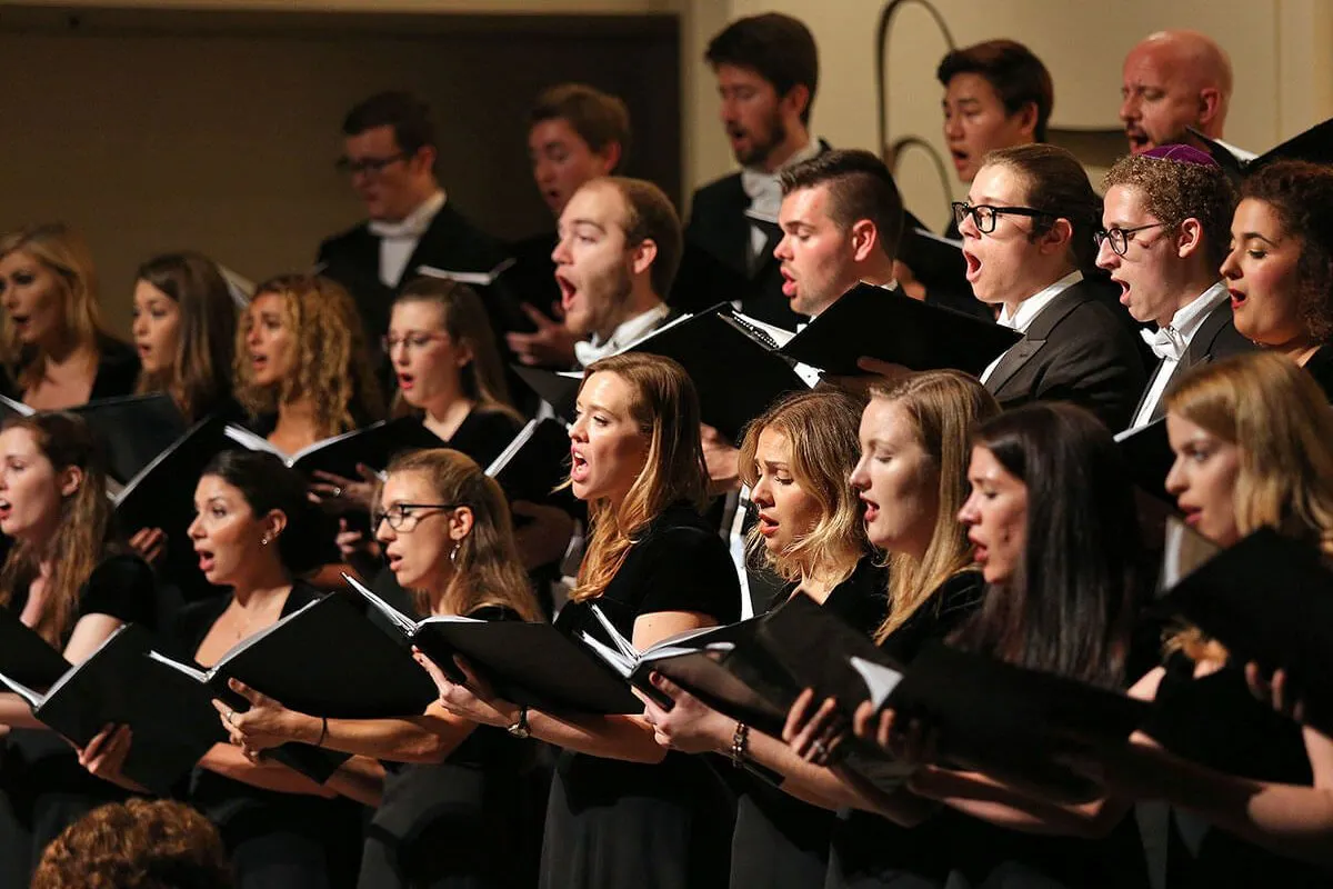 A group of singers performing onstage with choir books