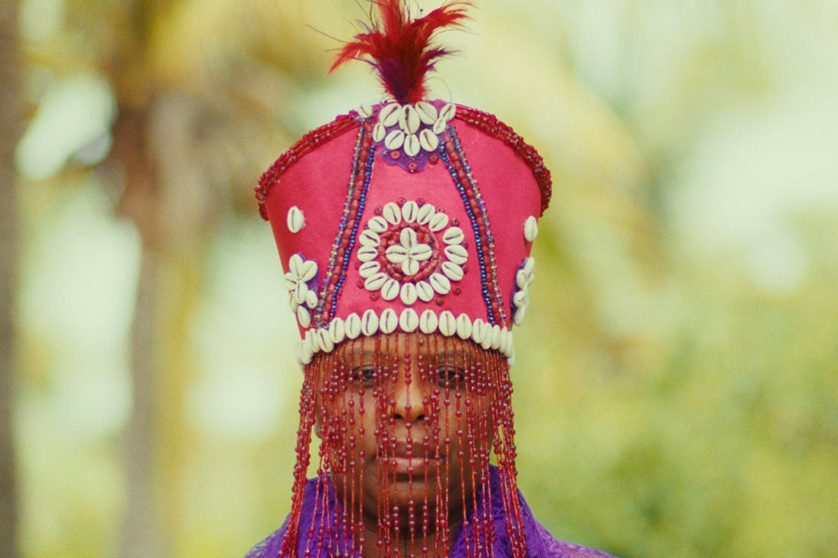Woman wearing a red crown with white cowries shells and a red beaded veil.