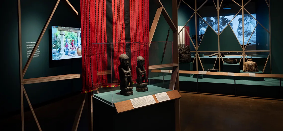 A selection of objects in the Fowler museum gallery, two in the foreground are small wooden statues