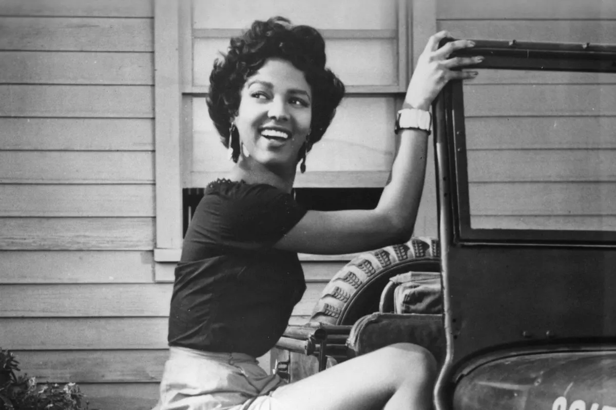 Dorothy Dandridge standing next to a car smiling