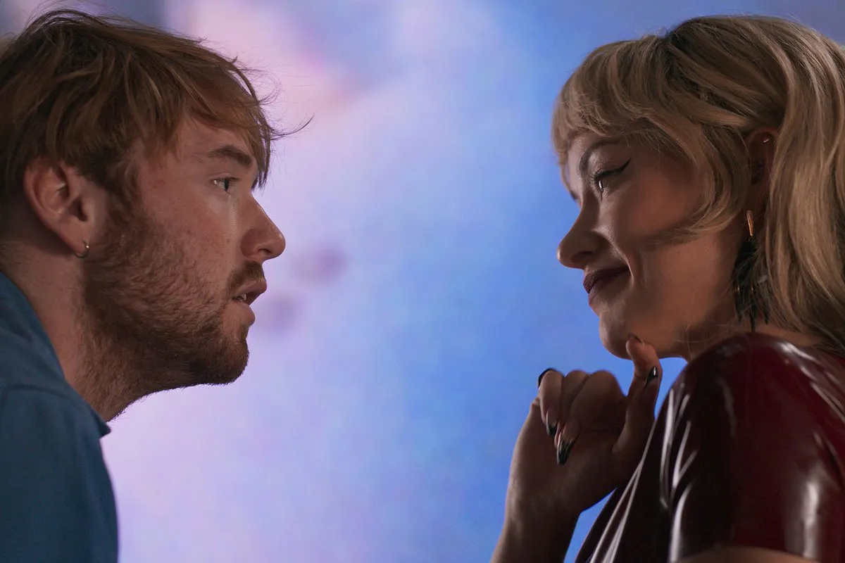 On the left, a man with short, scruffy blond hair and beard gazes into the eyes of a woman with wavy, blond hair