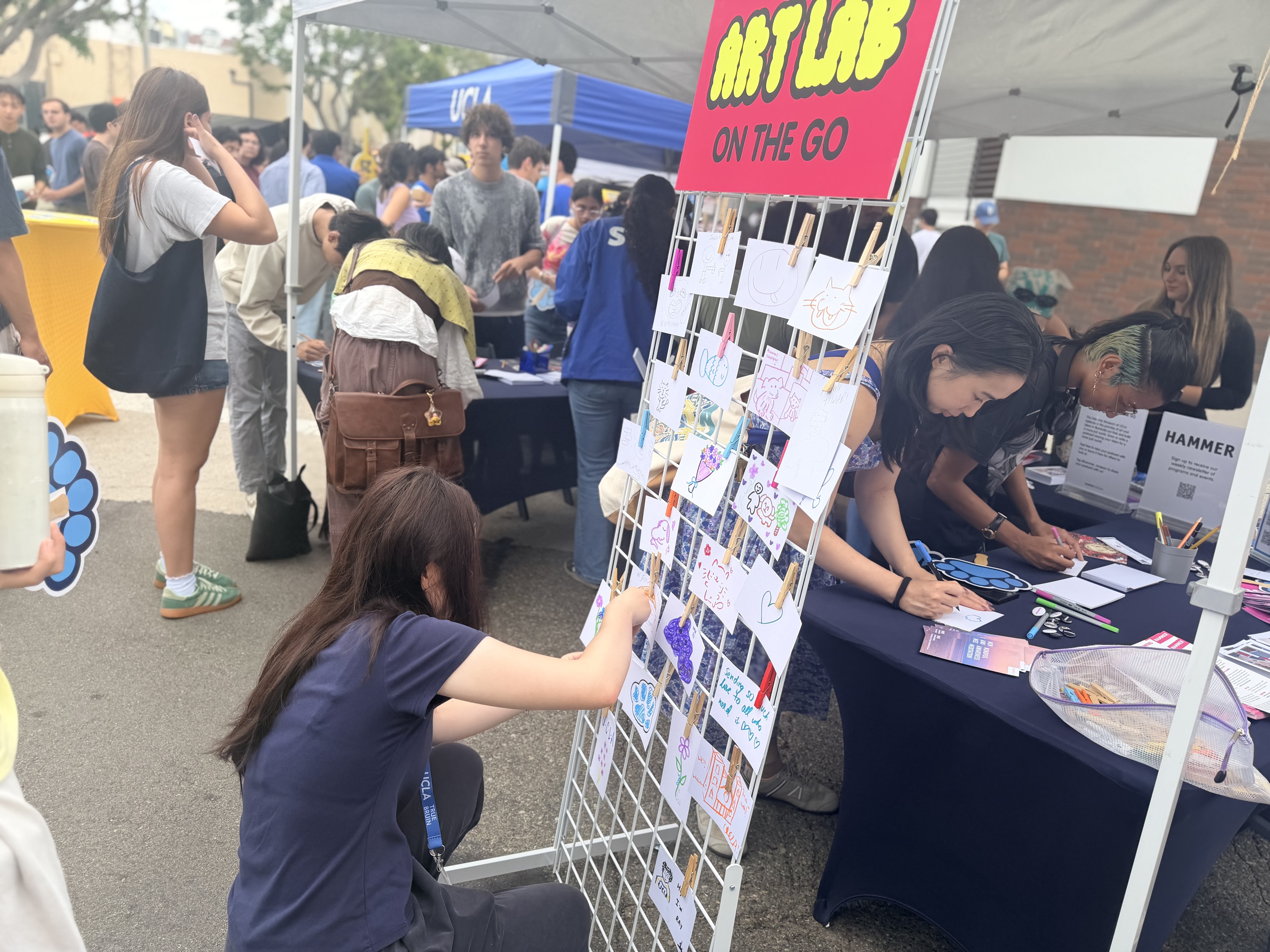 People add elements to a community artmaking display of personalized postcards