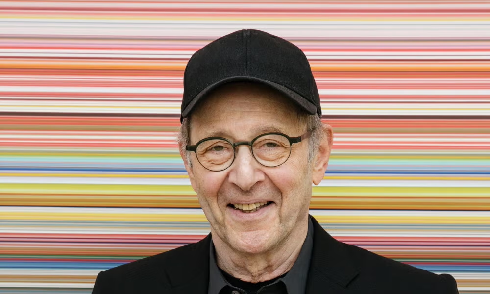 Portrait of steve reich posing against a colorful striped background