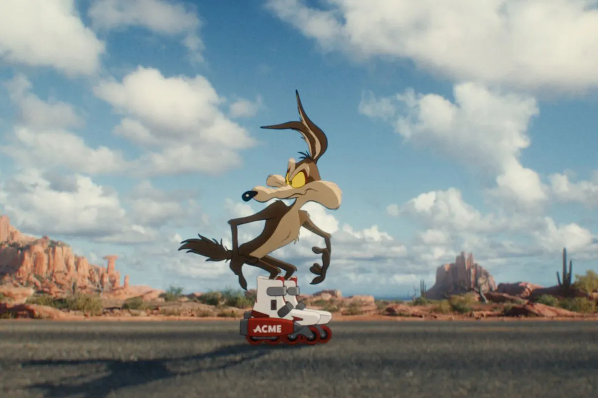 A cartoon coyote wearing ACME brand rollerblades stands on an empty desert highway
