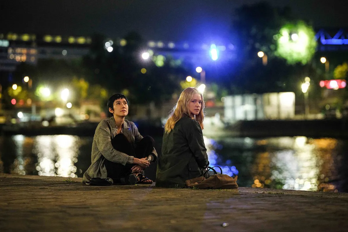 Two women sit on the waterfront, with city lights twinkling behind them