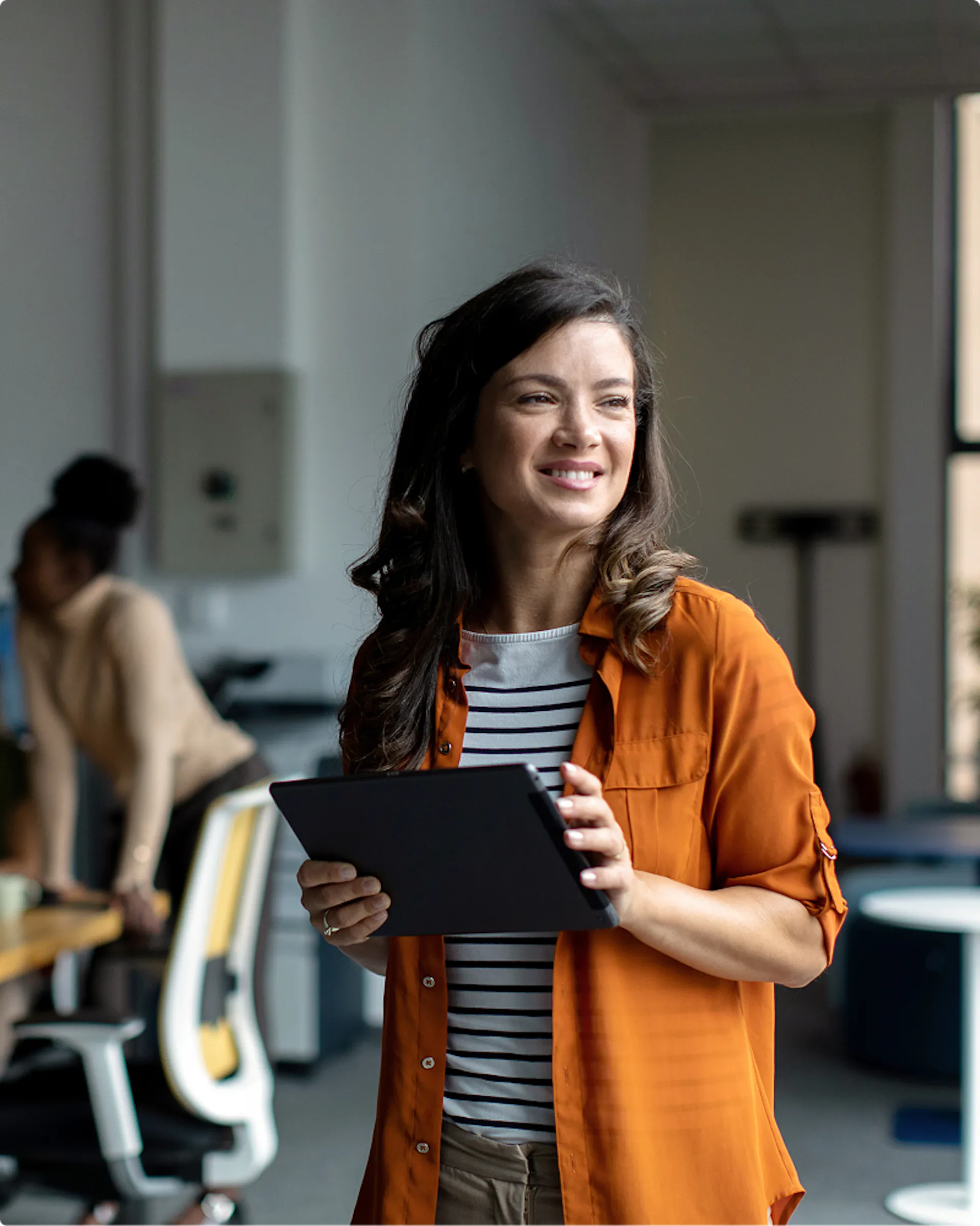 woman with an orange sweater smilling and holding a tablet