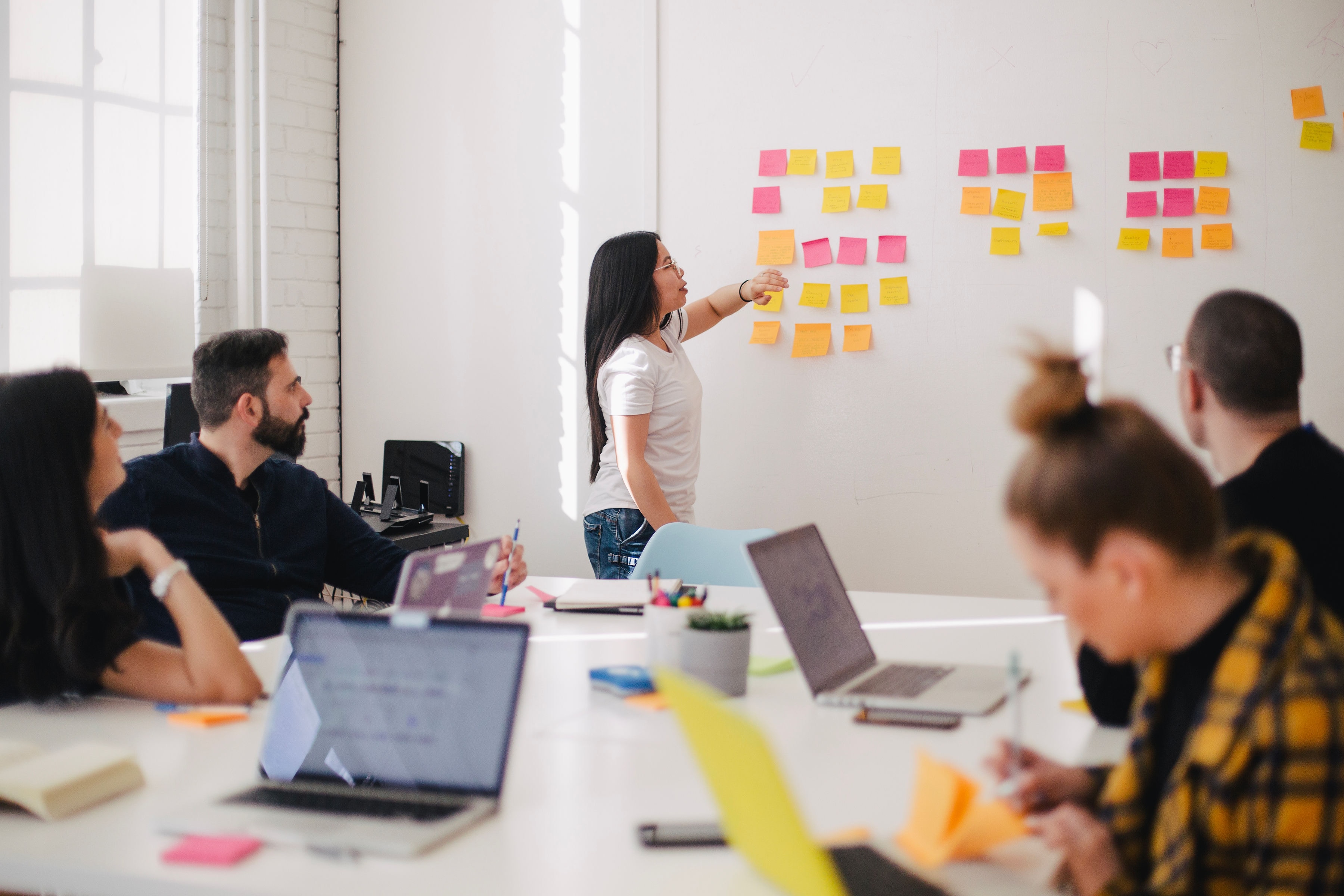 Woman putting post-it notes on a whiteboard while people watch