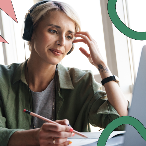 Woman with headphones on sitting in front of a laptop, writing notes