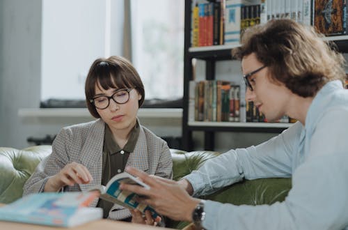Two people wearing glasses reading in a library.