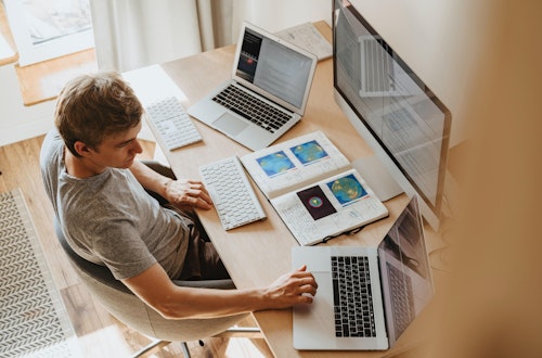 Man with two laptops and a desktop screen working at a desk. 