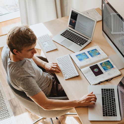 Man with two laptops and a desktop screen working at a desk. 