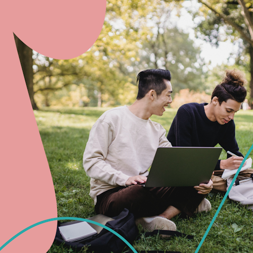 Two people sitting on a grassy field working on a laptop