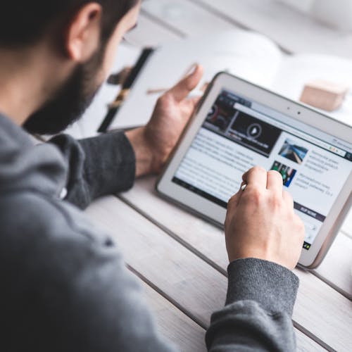 Man reading an article on his tablet with a cup of coffee next to him on the table.