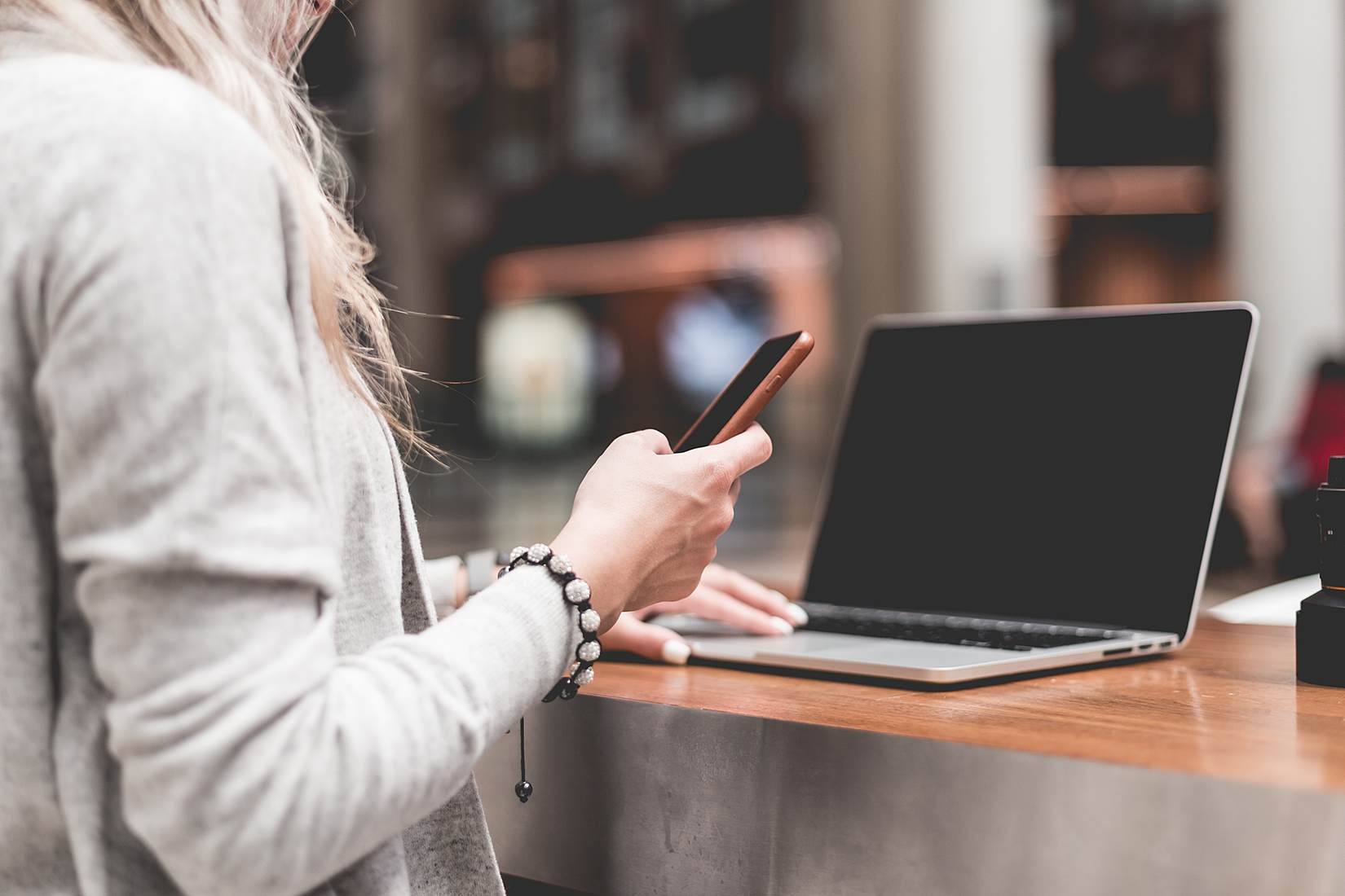 Woman checking her phone while typing on a laptop