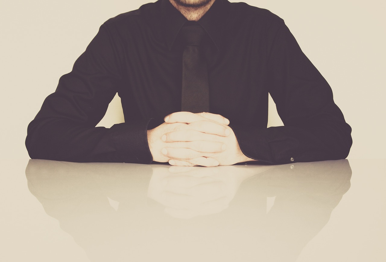 Man in a black suit sitting with arms folded