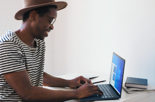 Man wearing a hat typing on his laptop