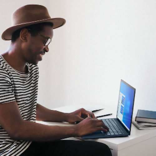 Man wearing a hat typing on his laptop