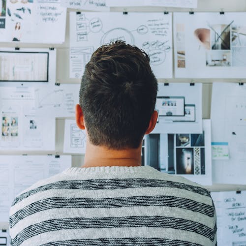 Man in striped shirt looking at papers taped to the wall.