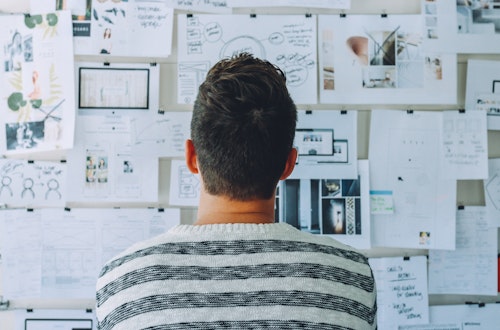 Man in striped shirt looking at papers taped to the wall, symbolising L&D mindset