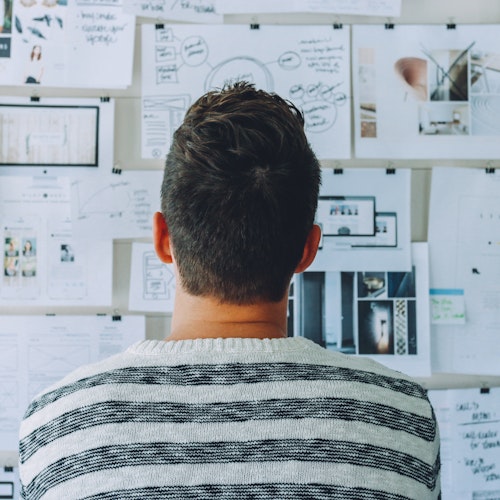 Man in striped shirt looking at papers taped to the wall, symbolising L&D mindset