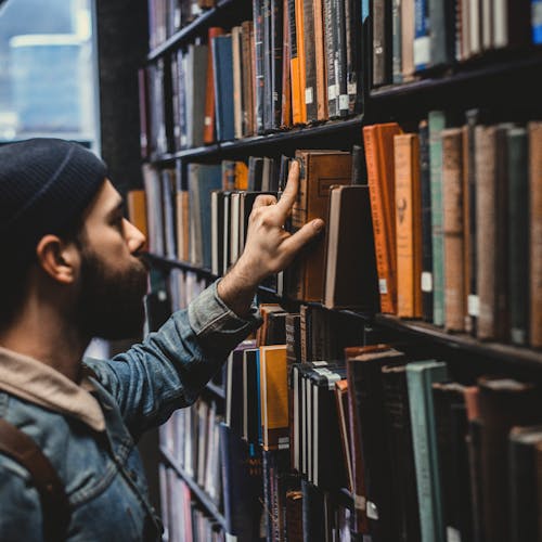 Man in a library reaching for a book