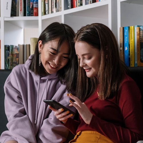 Young people sitting in a library looking at their phones, representing a generational divide