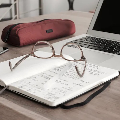 Glasses, notebook, and pencil case left in front of open laptop to symbolise developing a growth mindset