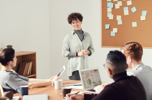 Woman standing up talking to a group of colleagues 