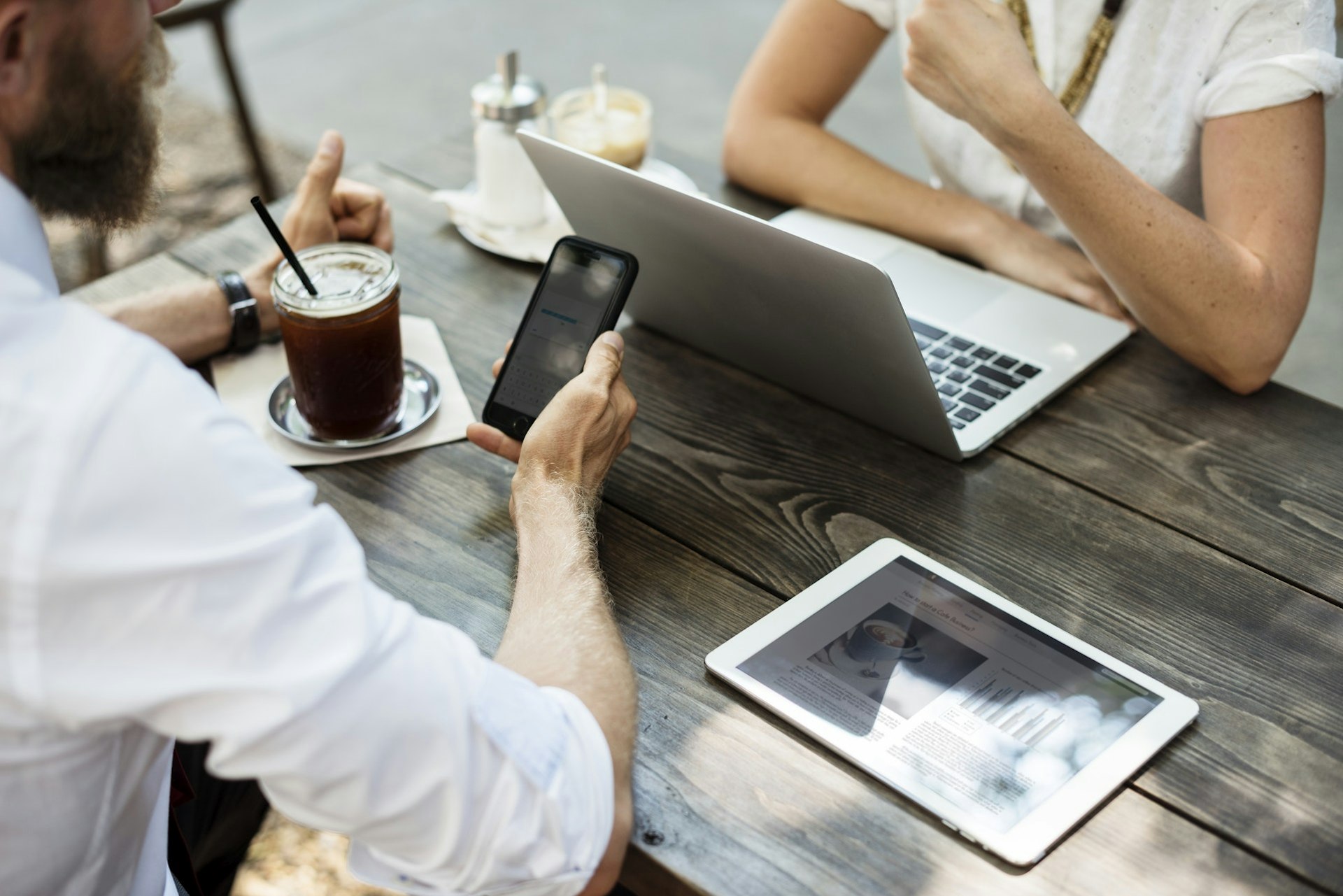 Two people sitting outside a cafe talking and working on their laptops