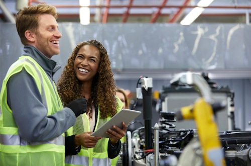 Two employees in a factory stand next to each other and laugh together