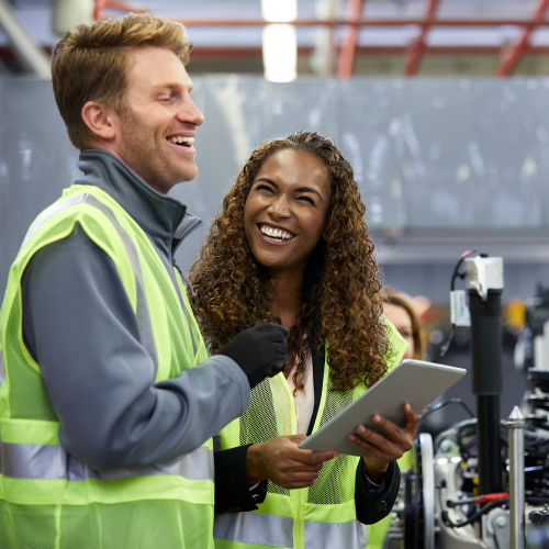 Two employees in a factory stand next to each other and laugh together