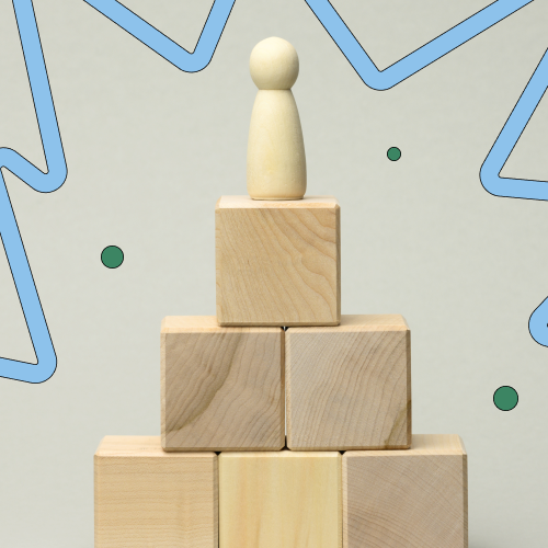 Wooden human figurine on top of a small pyramid of wooden blocks