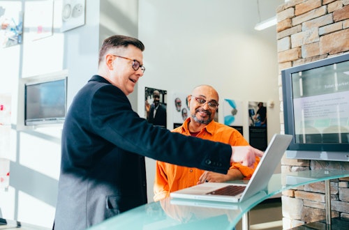 Two men wearing glasses looking at a laptop and pointing at the screen.