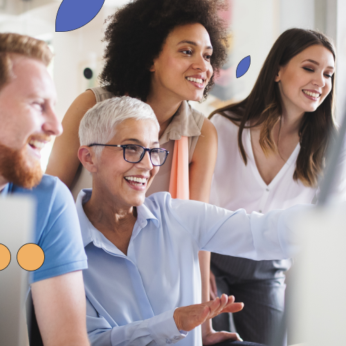 Four people sitting or standing around a computer smiling