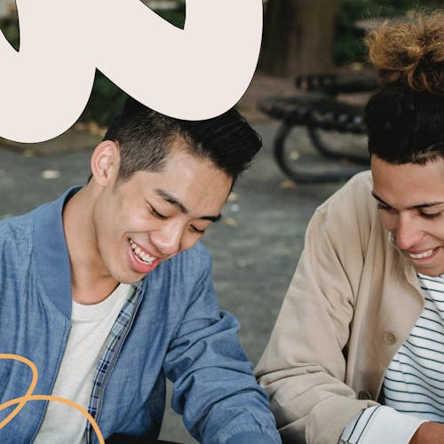 Two male friends sitting on a bench and writing in a notepad