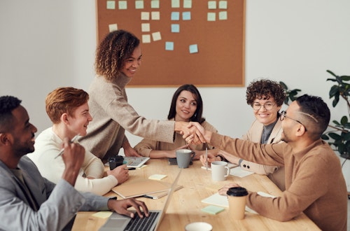 Diverse team sitting at a table working on a project, with two members shaking hands.