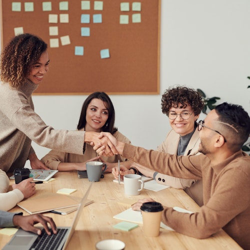 Diverse team sitting at a table working on a project, with two members shaking hands.