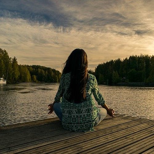 Woman sitting cross legged practicing mindfulness meditation in front of a lake.