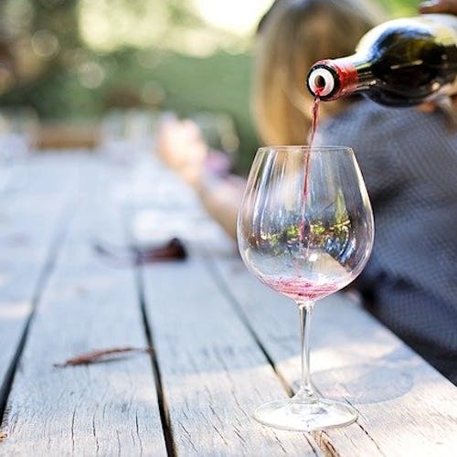 Red wine poured into a glass on a wooden table.