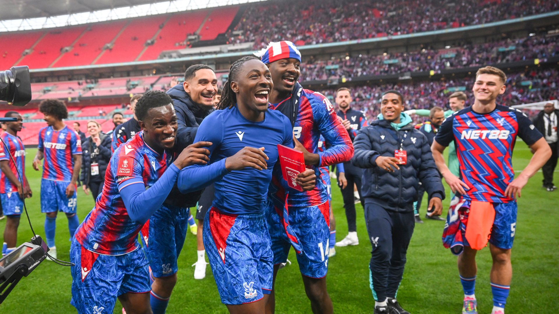 Eberechi Eze and Crystal Palace teammates, at Wembley, smiling and laughing in joy, after beating Manchester City to the FA Cup trophy in 2025. They are wearing the home jerseys of Crystal Palace, and Eze has his own off. 
