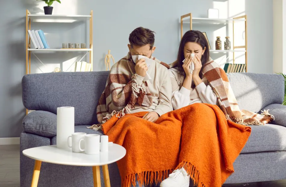 Young couple covered in blankets sitting on sofa at home with seasonal flu or cold. 