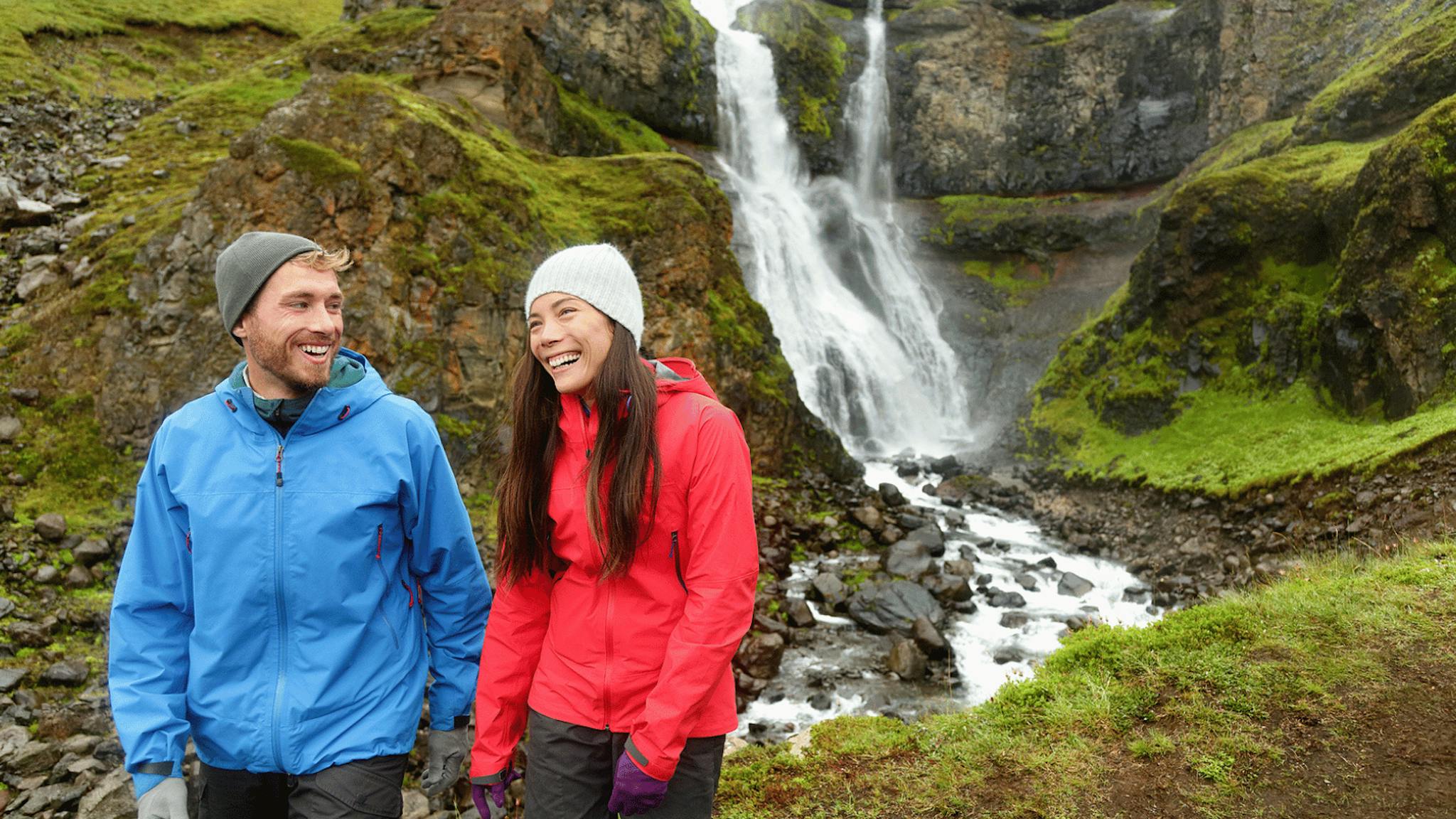 A couple smiling and hiking near a waterfall in Iceland.