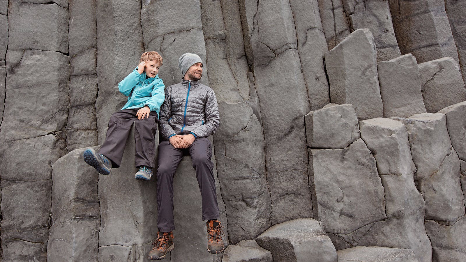 Father and son sitting on basalt columns in Iceland.