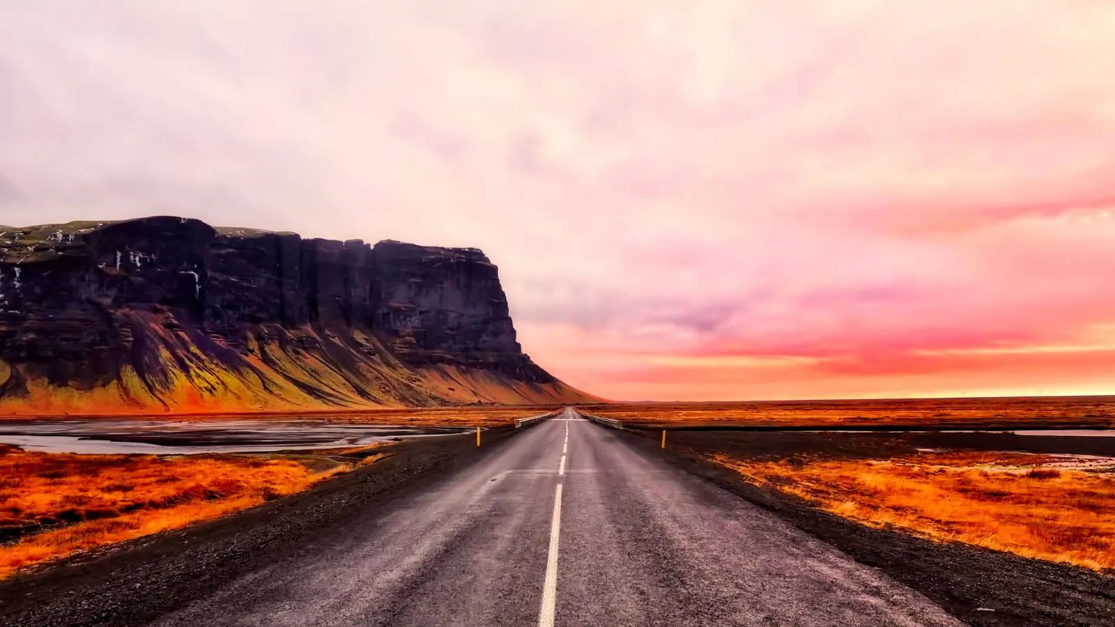 A highway in Iceland during a pink sunset with mountains in the background.