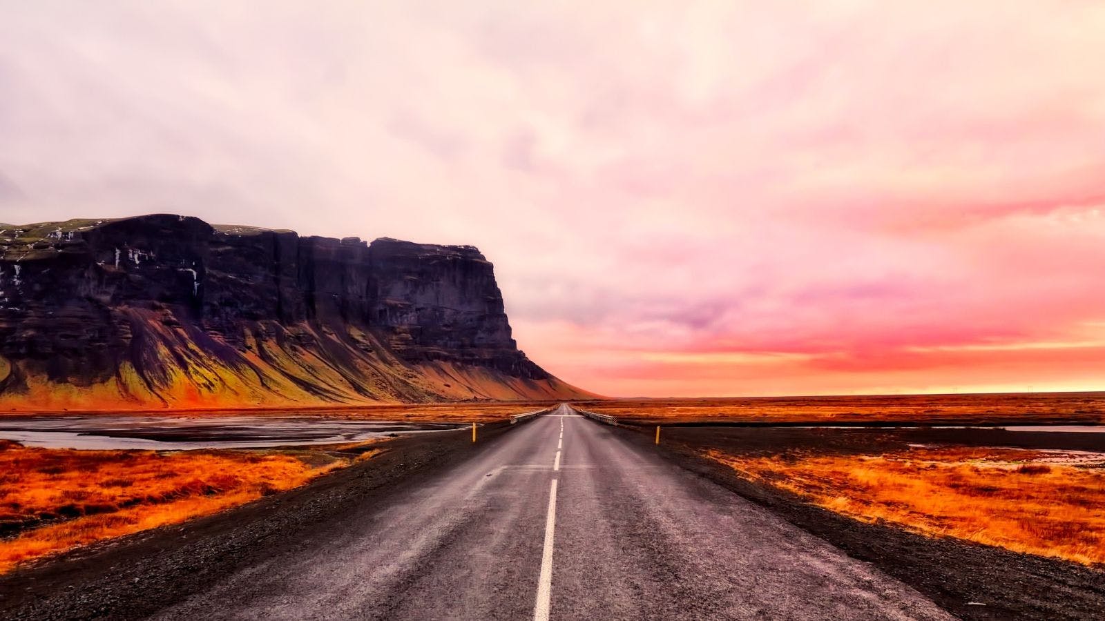 A highway in Iceland during a pink sunset with mountains in the background.